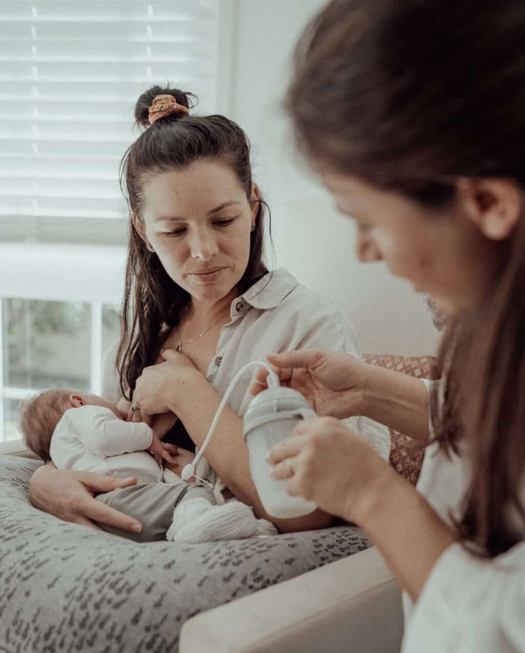 Postpartum doula supporting a mother who is breastfeeding using a supplementary feeding system