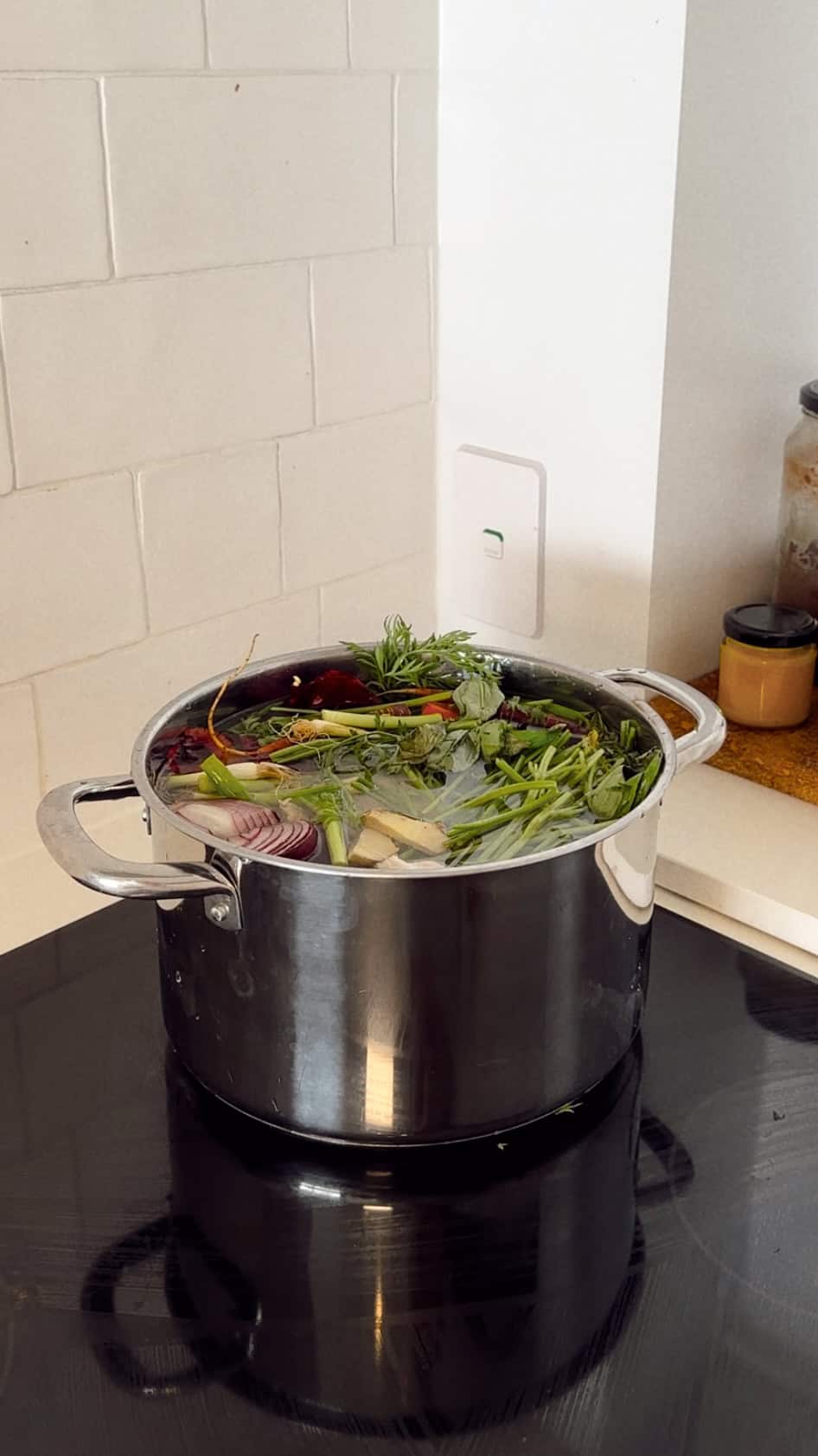 Village For Mama A pot on a stovetop filled with water, herbs, and vegetables, including onions and carrots.