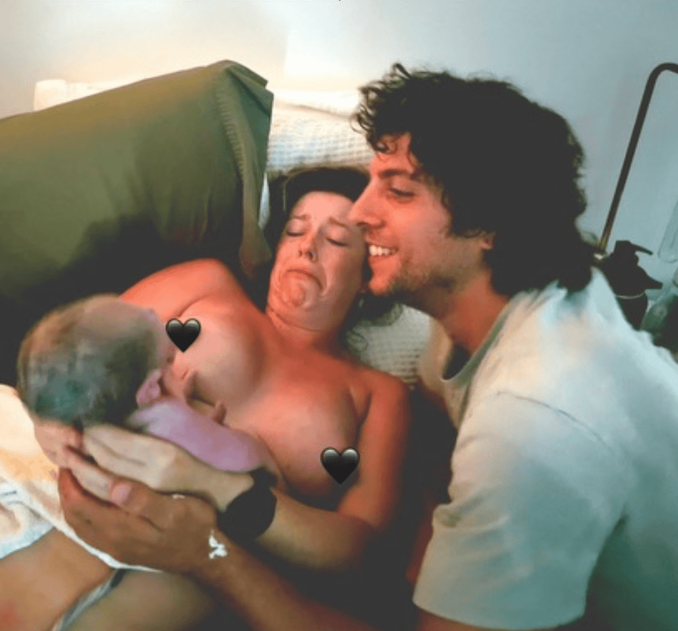Village For Mama A woman holding a newborn baby on a bed, with a man smiling beside her. Hearts cover parts of the image for privacy.