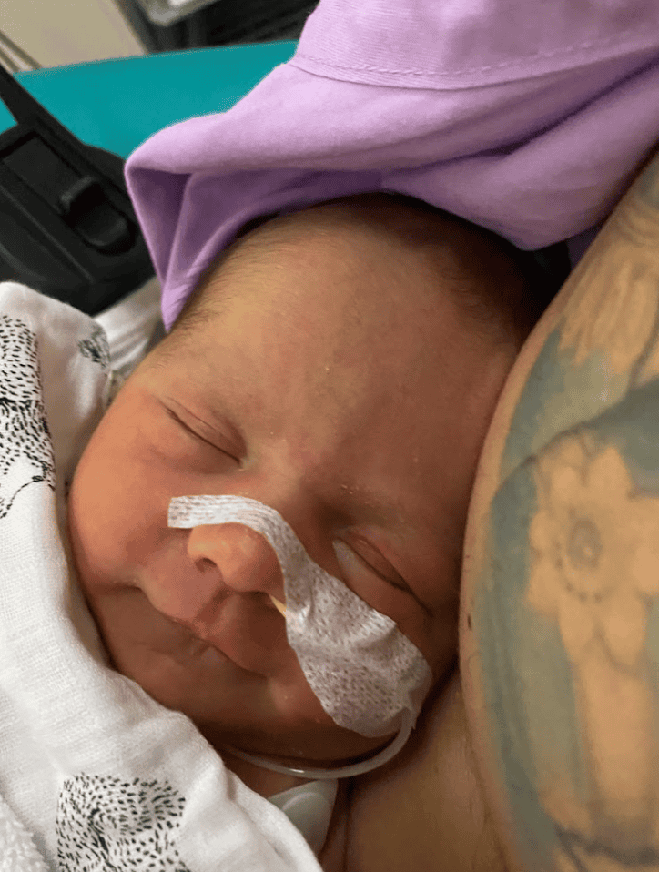 Village For Mama A newborn baby sleeps with a nasal tube and a floral tattoo visible on an adult's arm nearby.