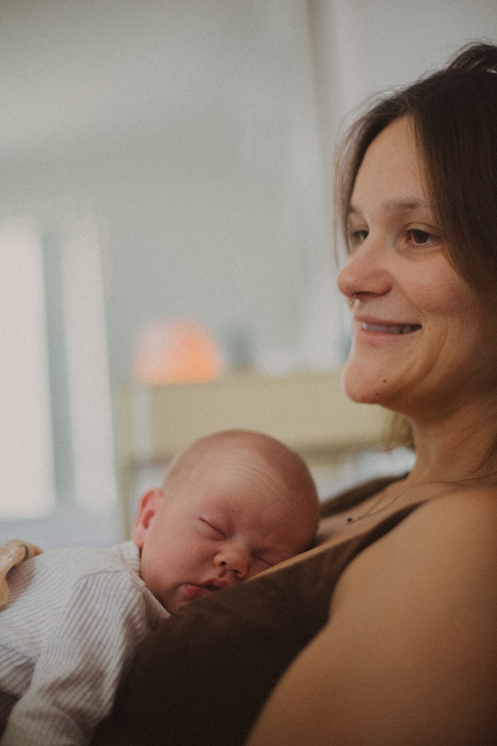 Village For Mama A woman smiles while a baby sleeps on her chest. The background is softly blurred.