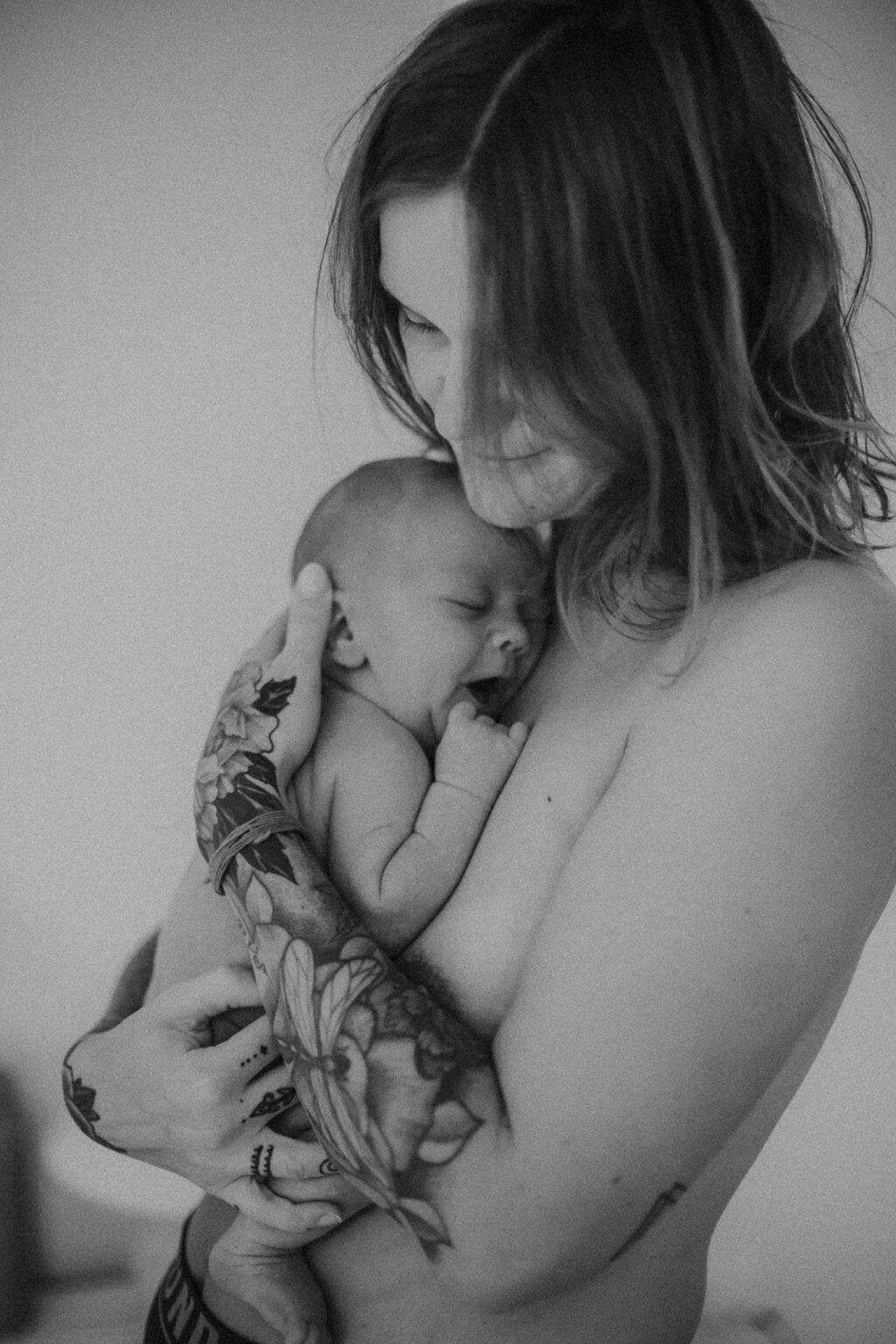 Village For Mama Black and white photo of a person with tattoos gently holding a sleeping baby against their chest.