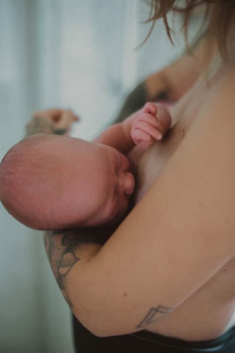 Village For Mama A newborn baby being held closely in the arms of an adult with tattoos.